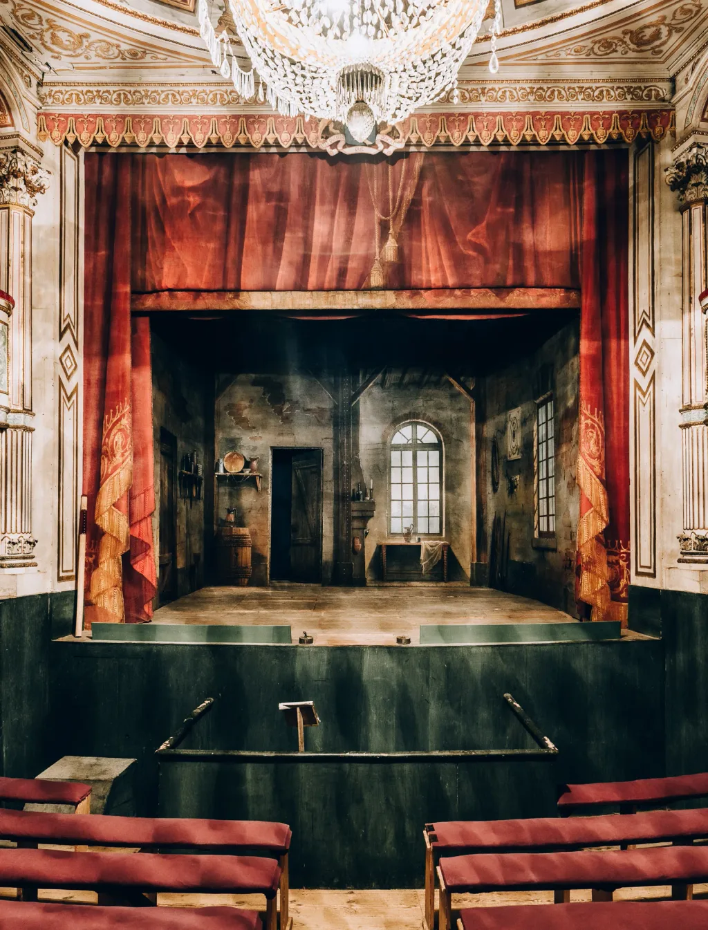 Small ornate theatre with red seats, a painted stage and chandelier at Chateau de Digoine