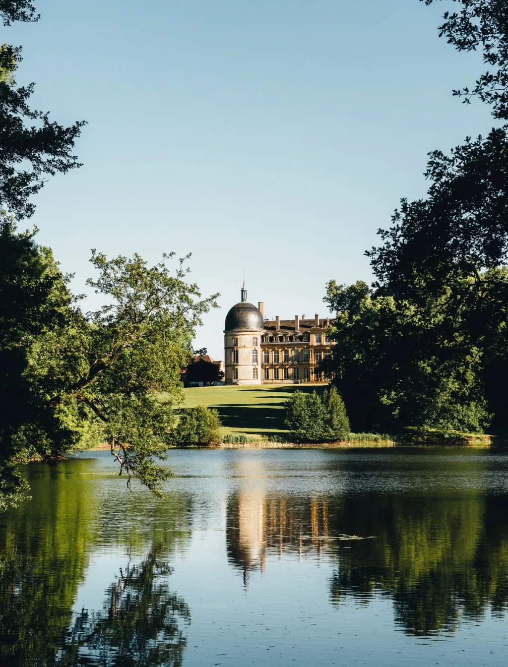 Chateau de Digoine seen beyond a tree-lined pond, its towers reflected in still water