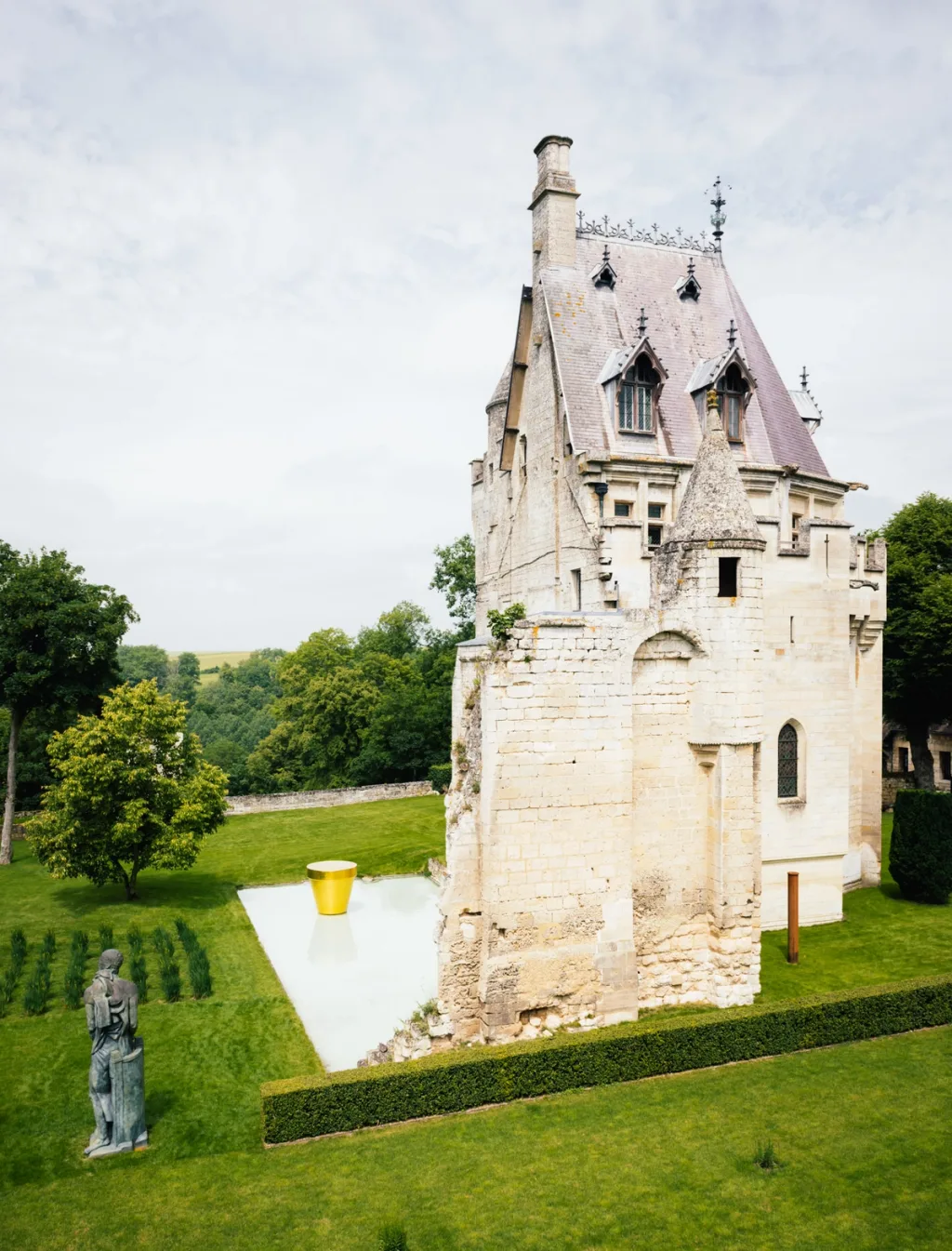 Steep-roofed tower and sculptures among rectangular garden plots at Donjon de Vez