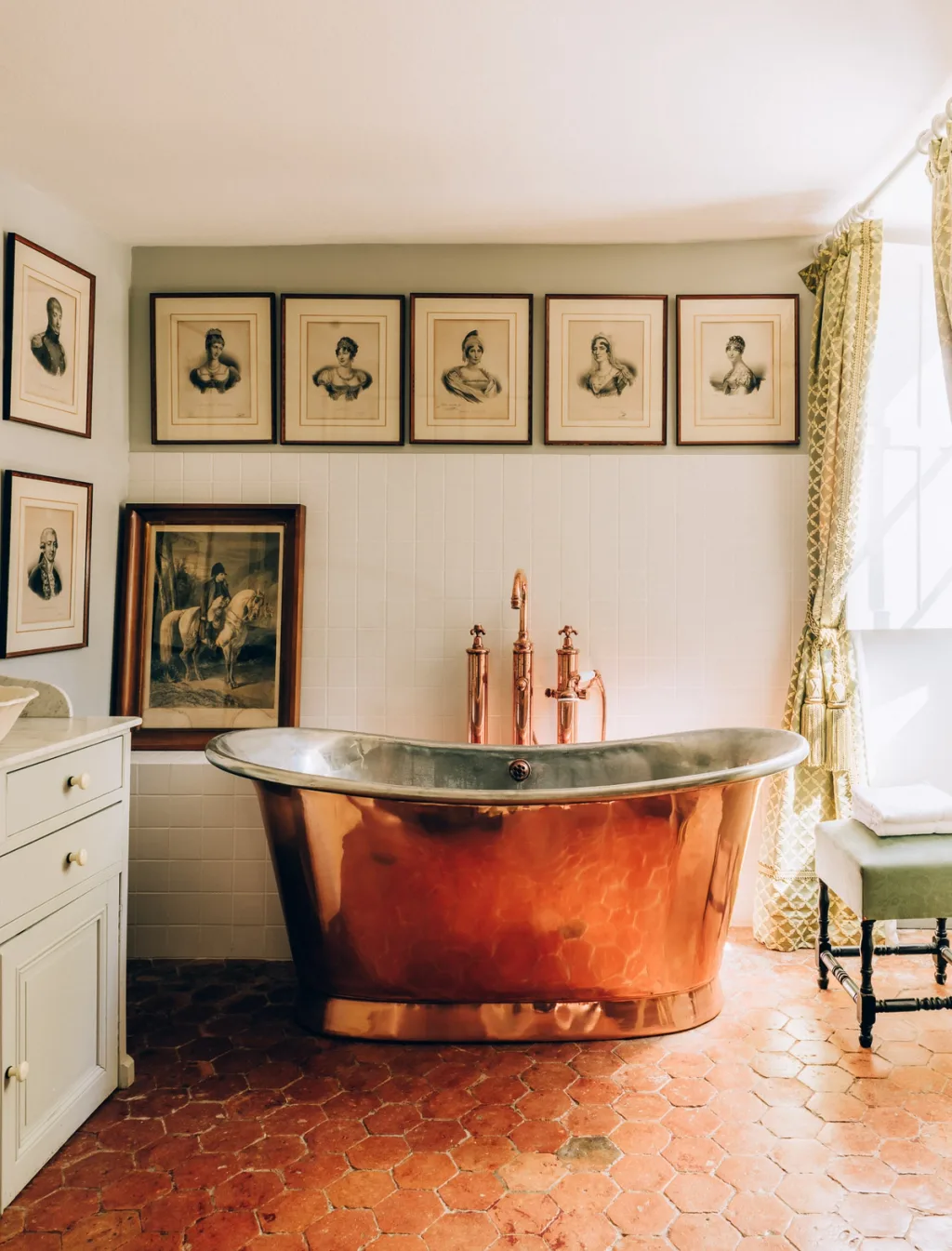 Copper-toned bathtub beneath a row of framed portraits at Chateau de Digoine