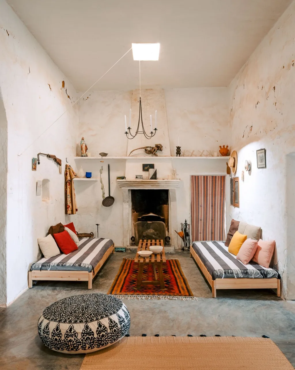 Striped daybeds face each other beside a fireplace in a white-walled Almeria living room