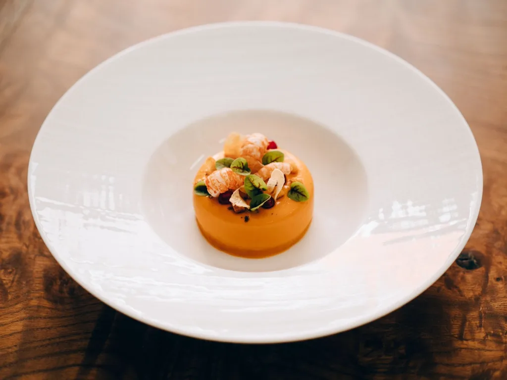 Orange cylindrical dish with a delicate garnish on a wide white plate in a Lyon restaurant