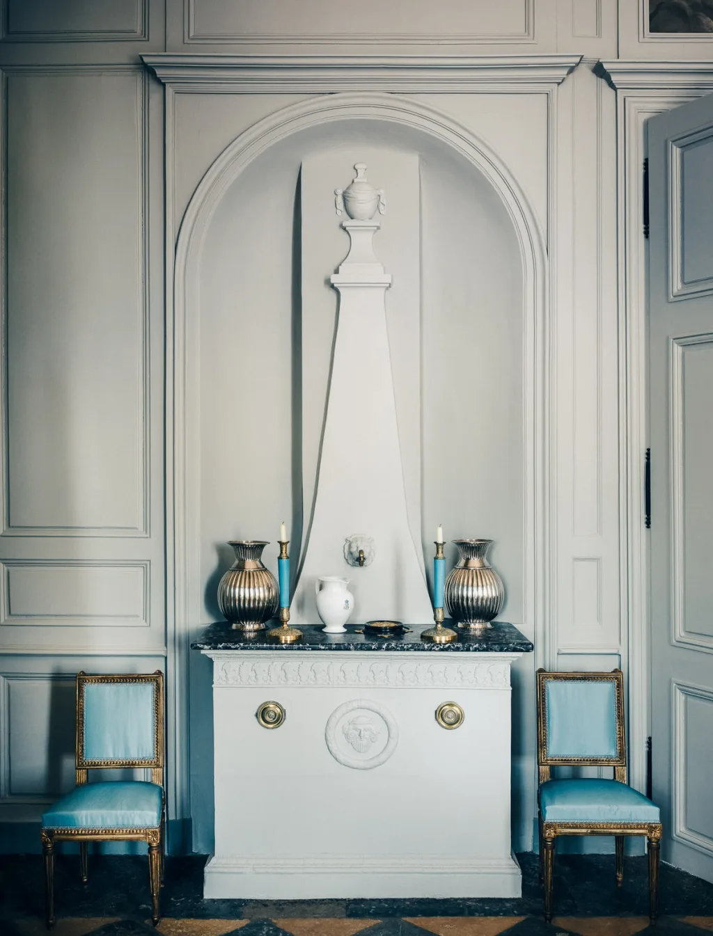 White ornamental fountain flanked by blue chairs in a panelled room at Chateau de Digoine
