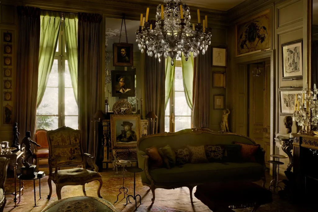 Green salon with a sparkling chandelier, ornate seating and layered portraits, Pierre Bergé, Paris