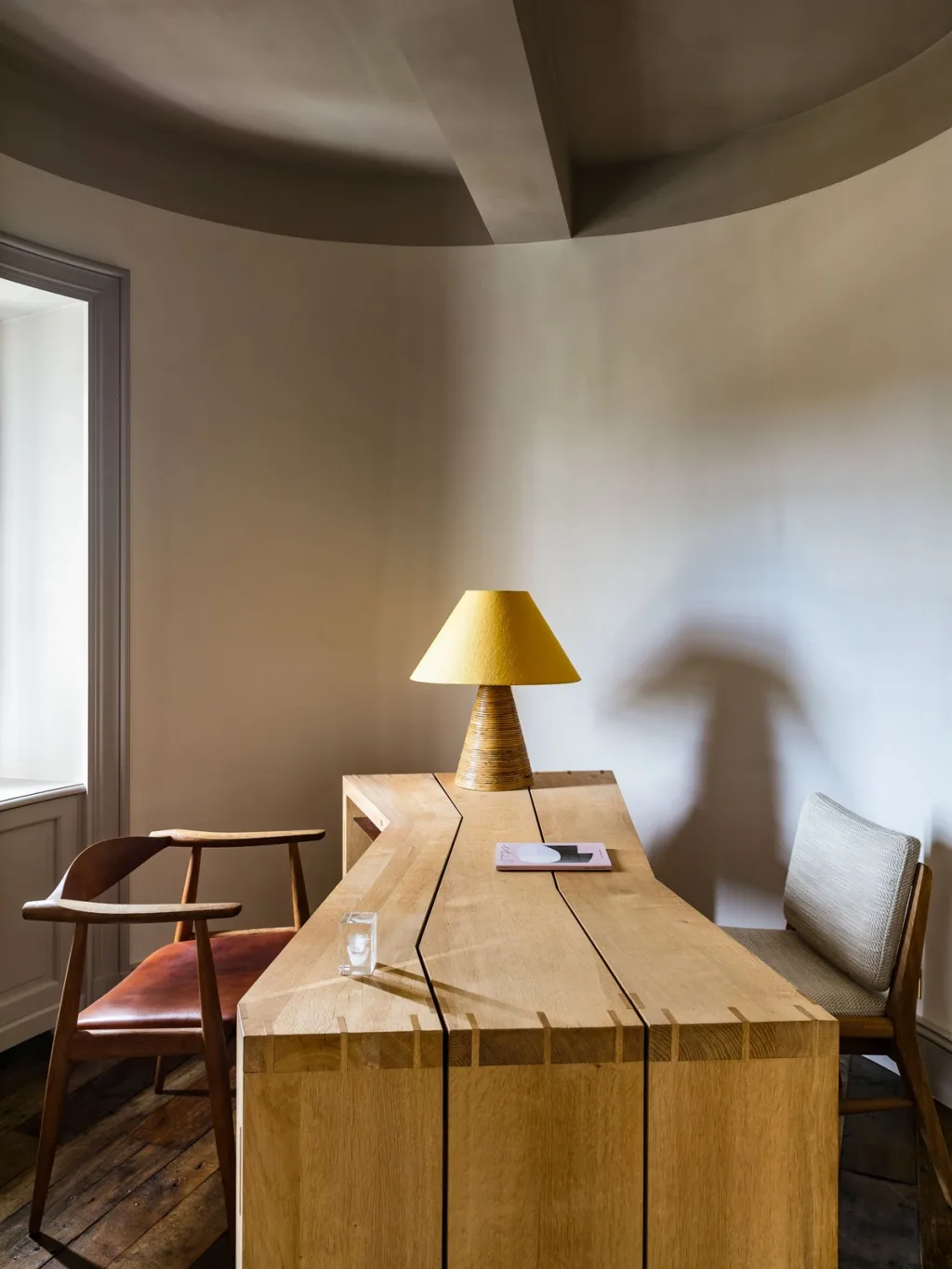 Slab-like wooden desk with a yellow lamp in a curved room at Fabrègues, Pierre Yovanovitch