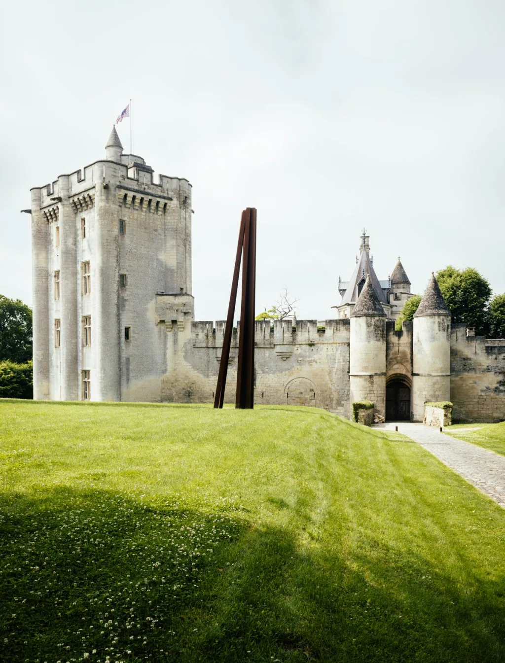 Tall angular sculpture on a green lawn before the fortified walls of Donjon de Vez