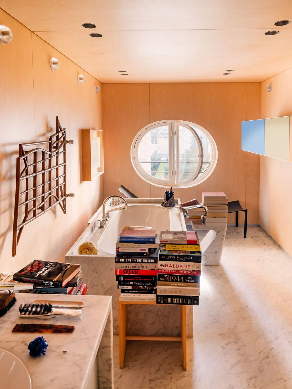 Wood-lined bathroom with books and a round window in Laurent Buttazzoni's Paris interior