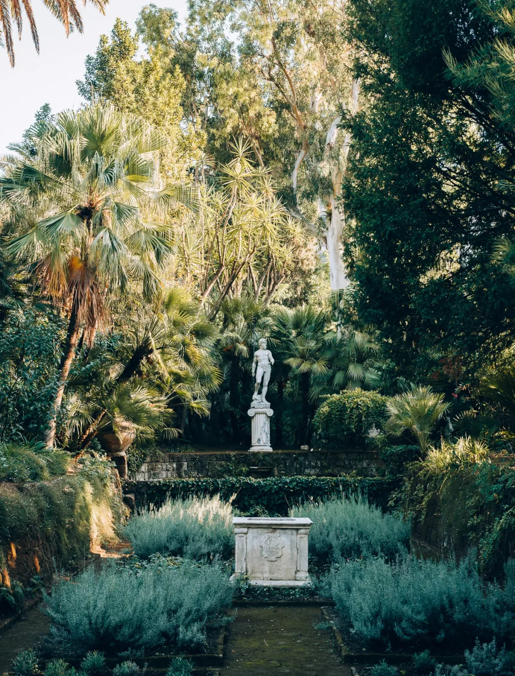 Statue and carved stone pedestal along a path through the lush gardens of Villa Astor