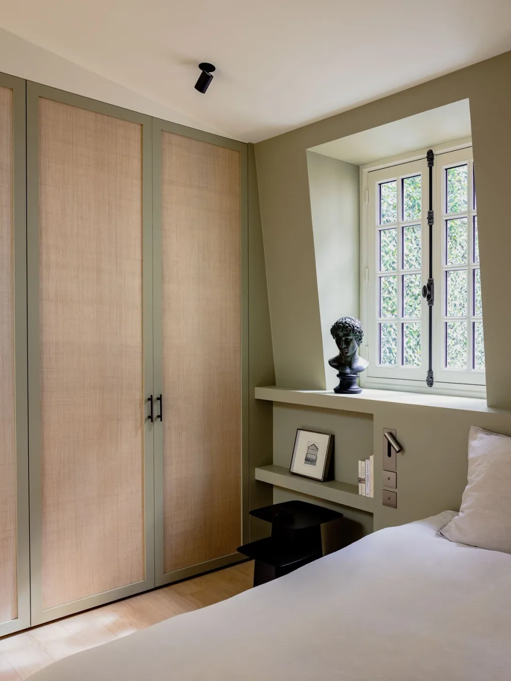 Muted green bedroom with tall wardrobes and a window bust in Hugues de Blignières' Paris interior