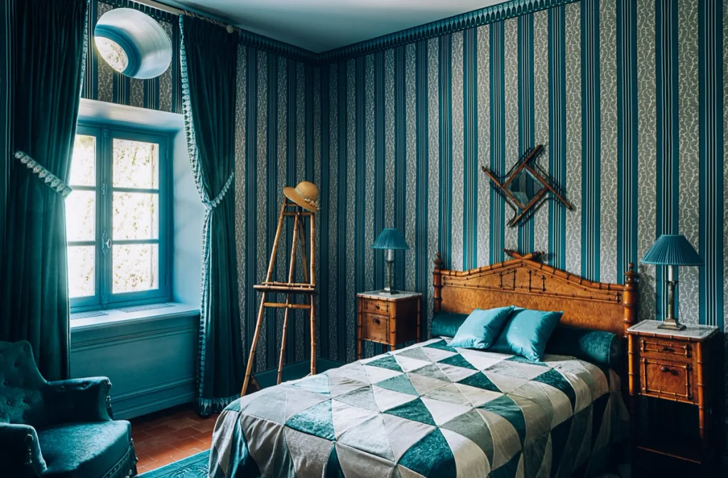 Turquoise striped bedroom with a wooden bed and geometric quilt at Dior, la Colle Noire