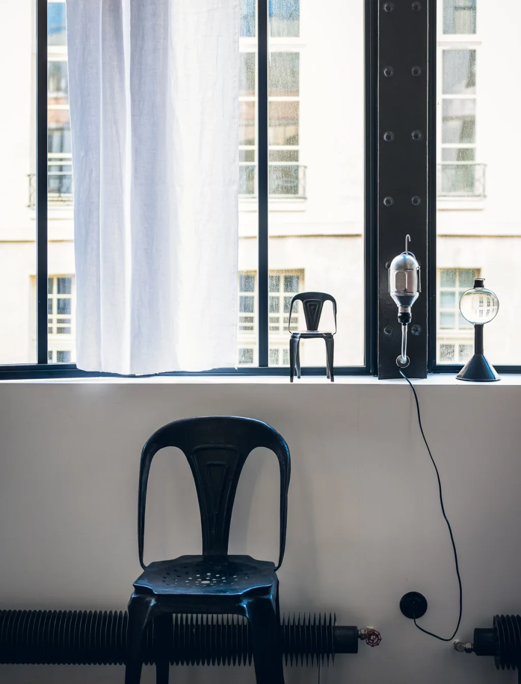 Black chair below a miniature chair and lamps on a windowsill at Daniel Rozensztroch's Paris home