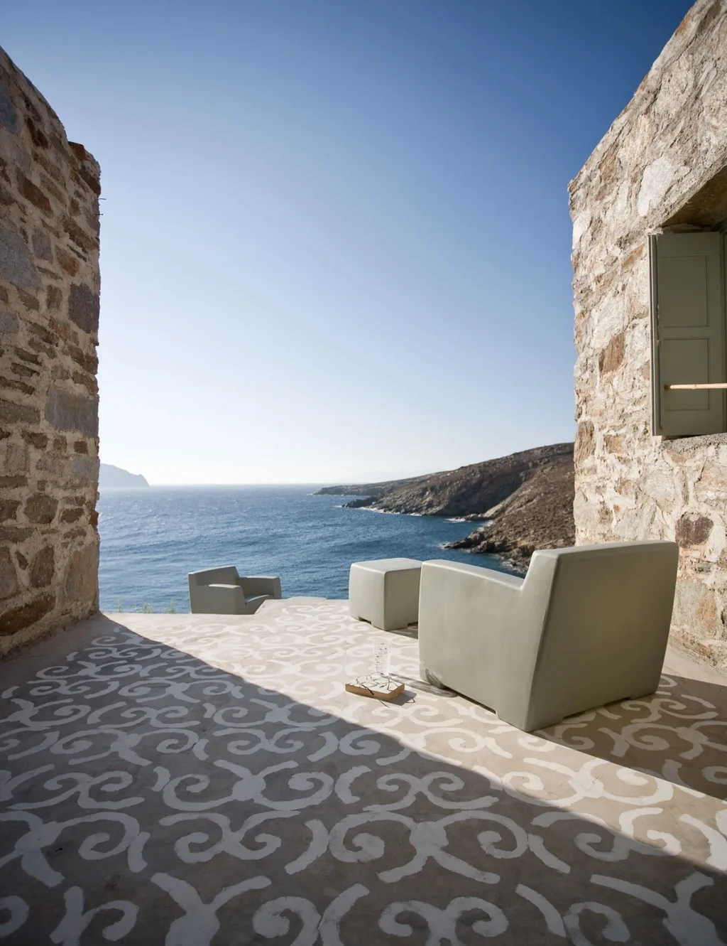 Pale armchairs on a patterned terrace between stone walls overlooking the sea, Paola Navone, Serifos