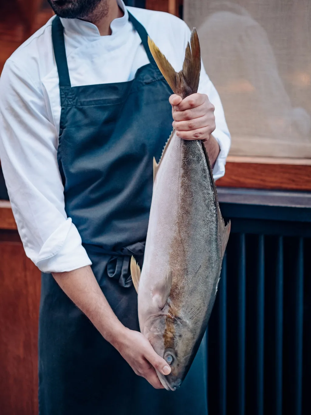 A cook in a dark apron holding a large whole fish for Cyril Lignac’s Saisons cookbook