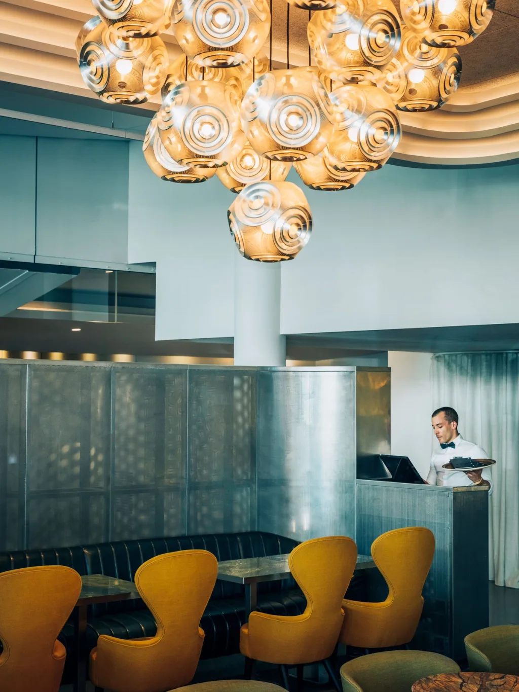 Waiter serving beneath a cluster of woven metallic pendant lamps, Pullman Bercy hotel