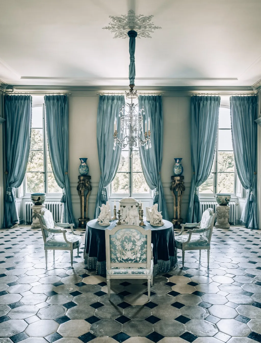 Round dining table with pale blue chairs and tall blue curtains at Chateau de Digoine