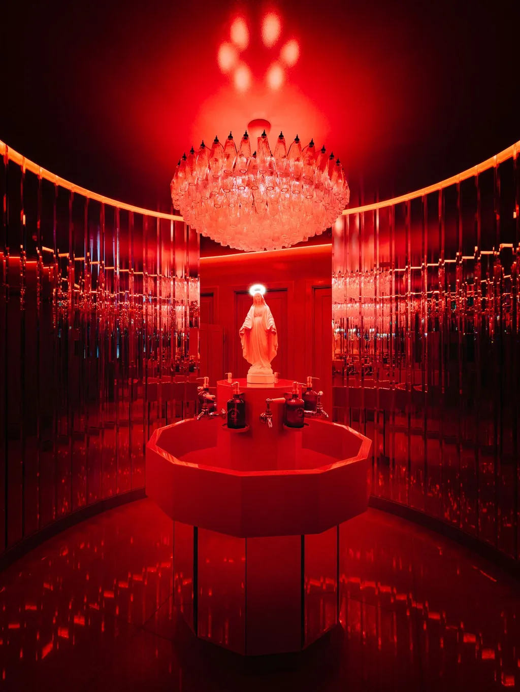 Red-lit washroom with a central basin, statue and chandelier at Big Mamma, UK