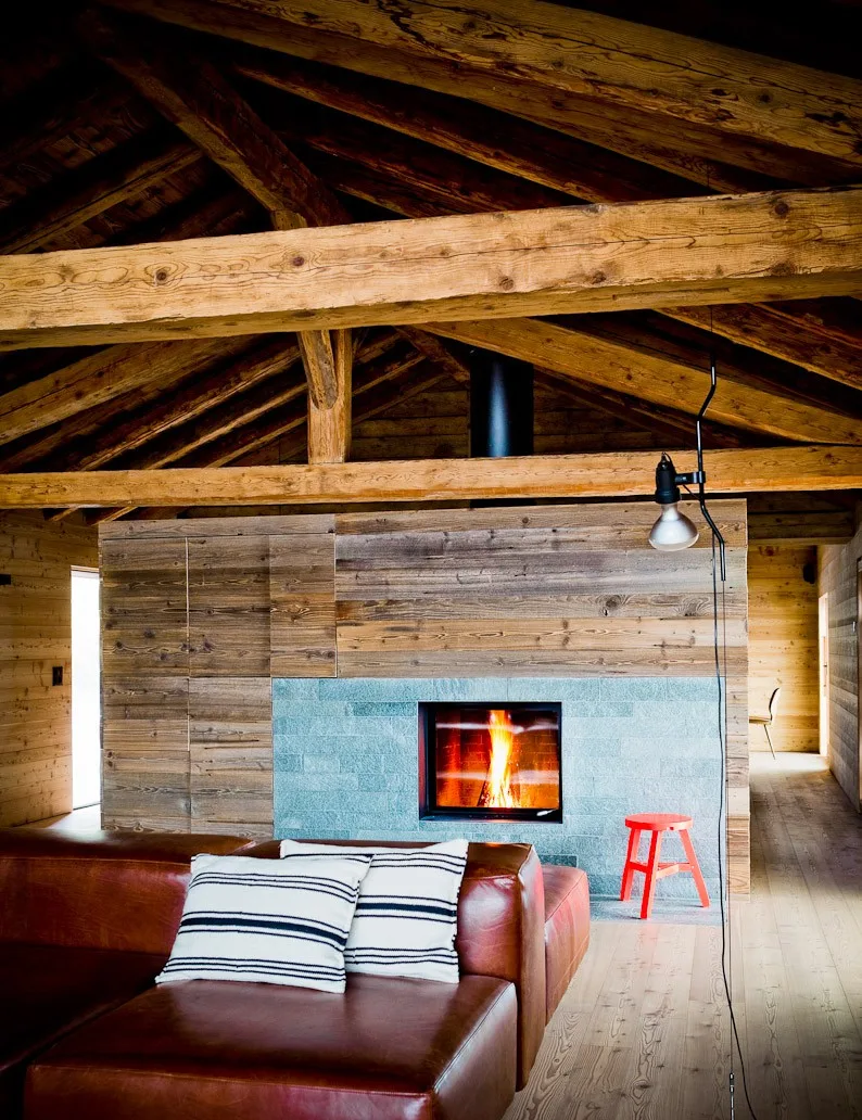 Timber-framed lounge with a stone fireplace and leather sofa at Montagne Alternative hotel, Switzerland