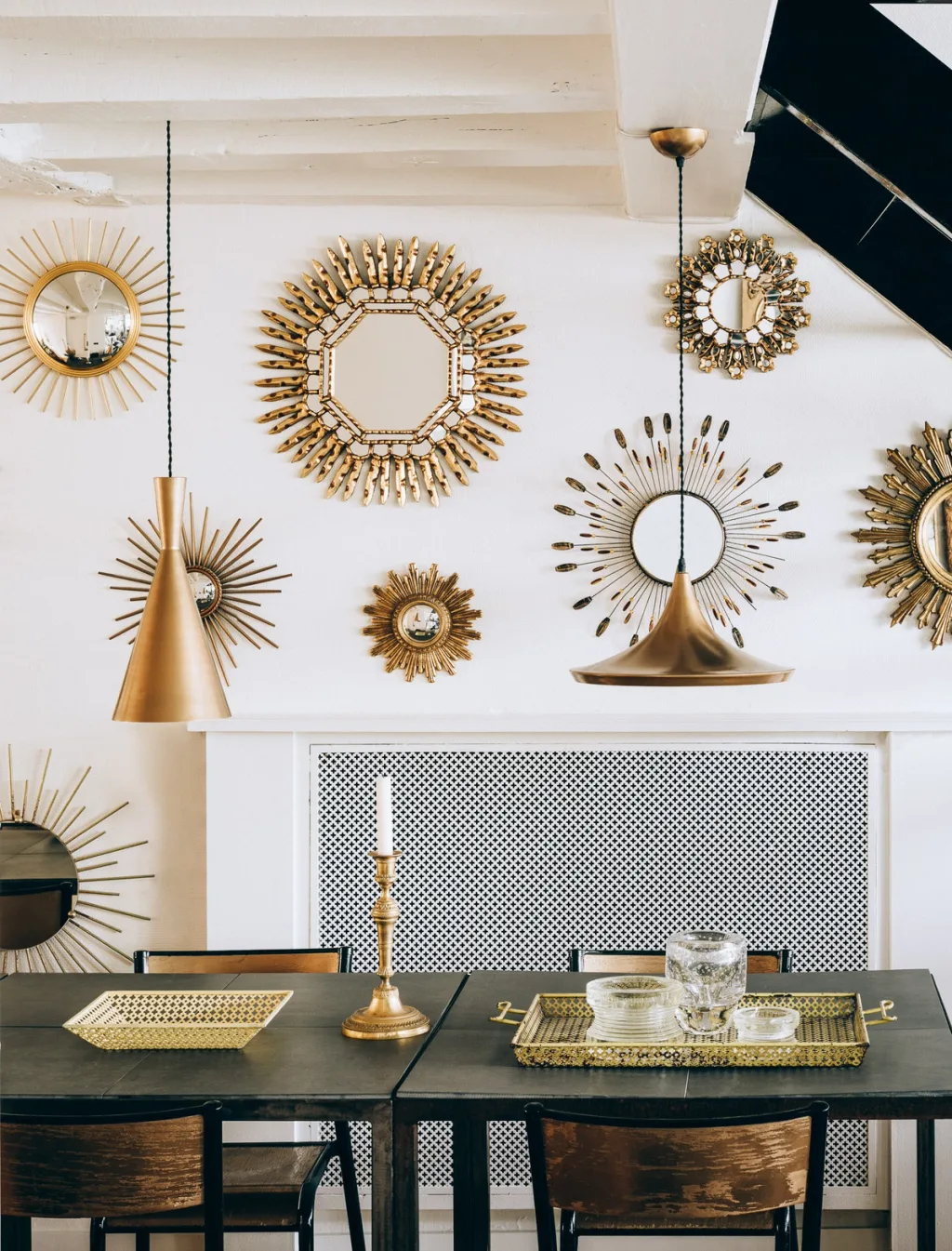 Collection of gold sunburst mirrors above a dark dining table, Michel Klein, Paris