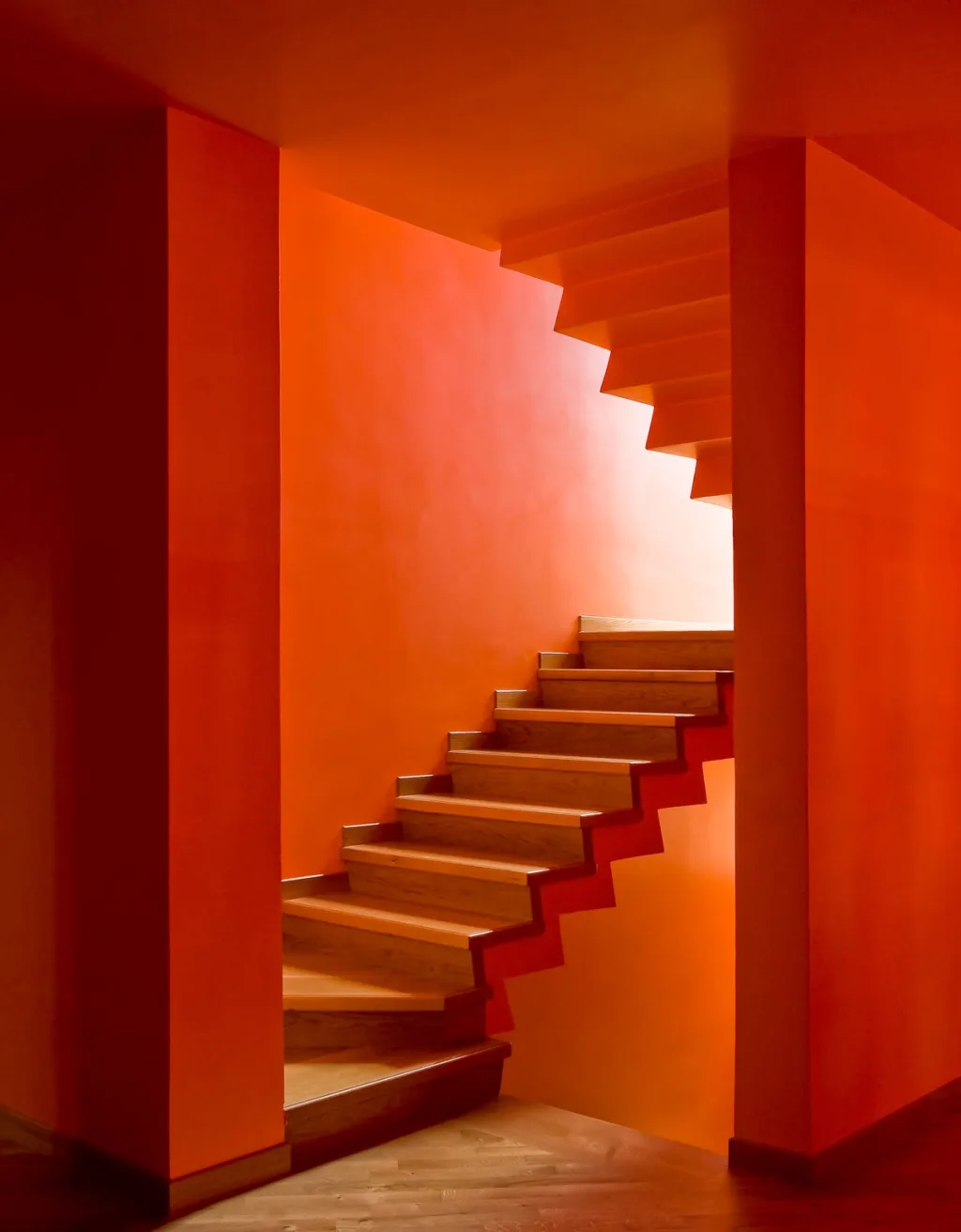 Angular staircase rising between vivid orange walls in the Maurizio Galante interior, Latina