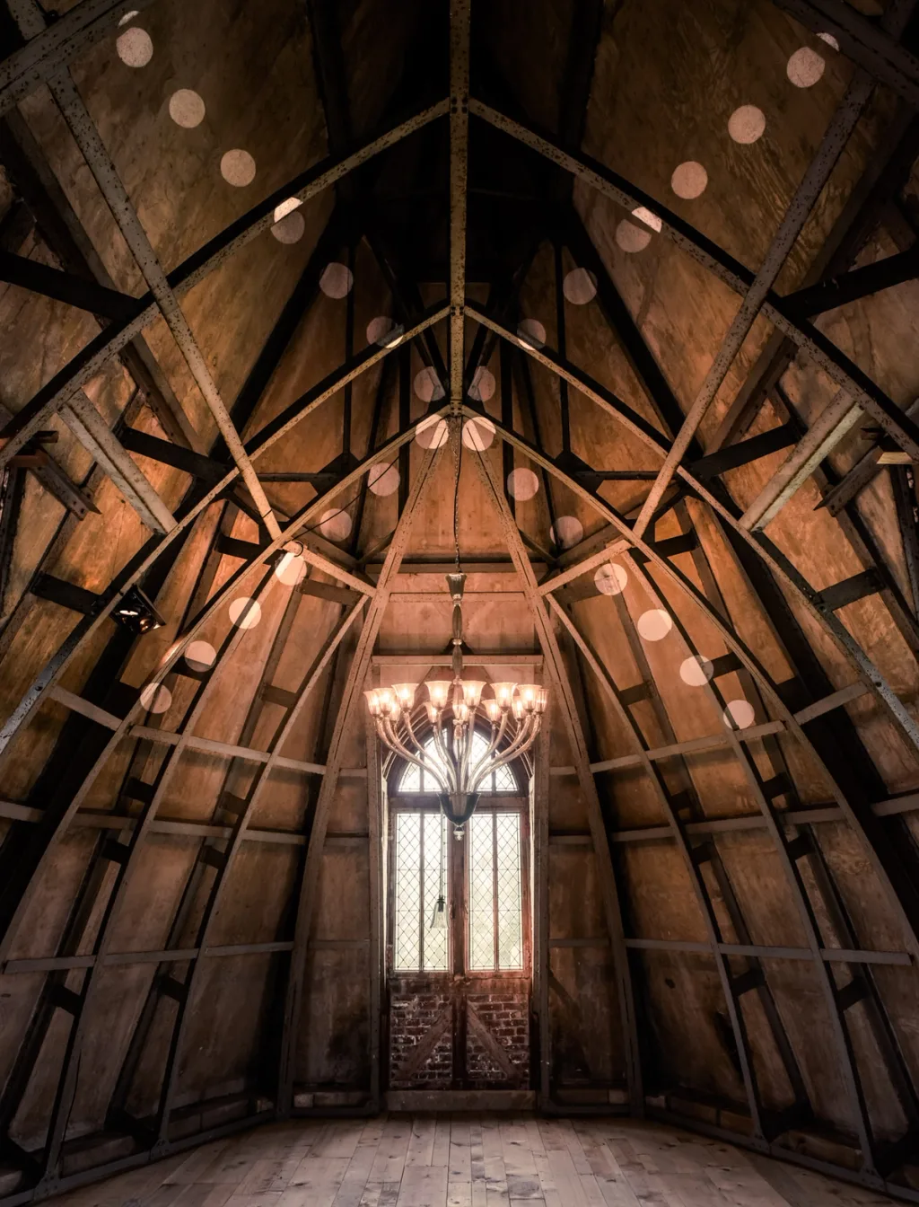 Exposed timber roof with suspended discs and a chandelier at Donjon de Vez