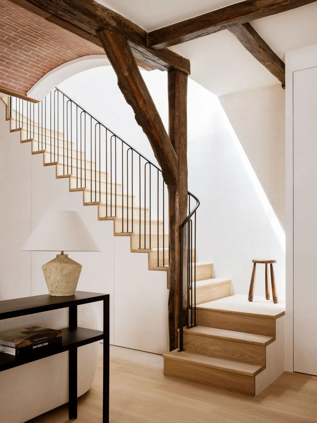 Wooden stairs and slender black railings beside old beams in a Hugues de Blignières interior, Paris