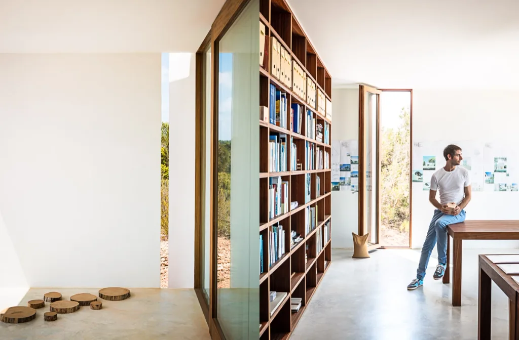 Wooden discs by a glazed wall paired with a man beside library shelves at Casa Formentera, Marià Castello