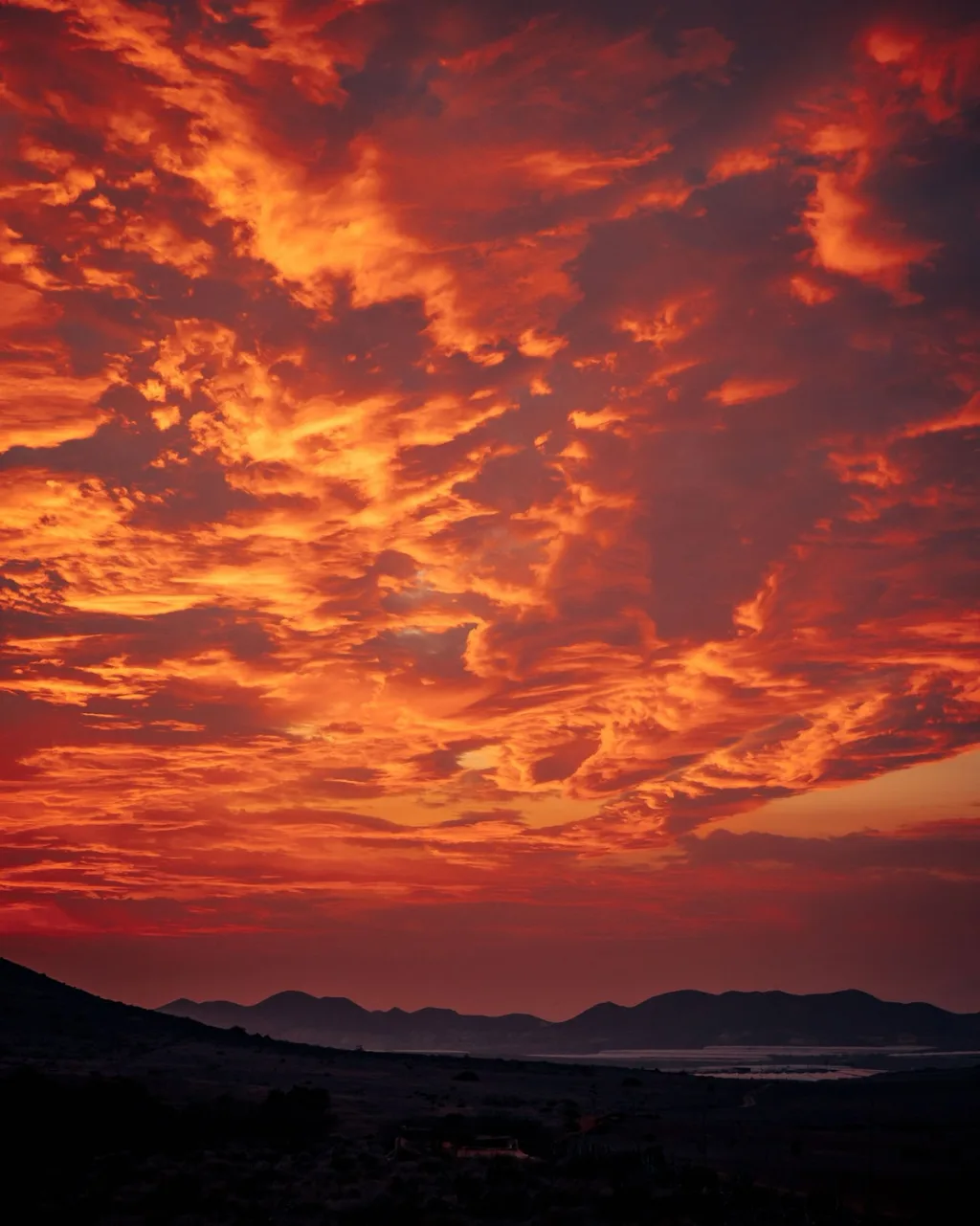 Fiery orange sunset clouds above dark mountain silhouettes and the coast in Almeria