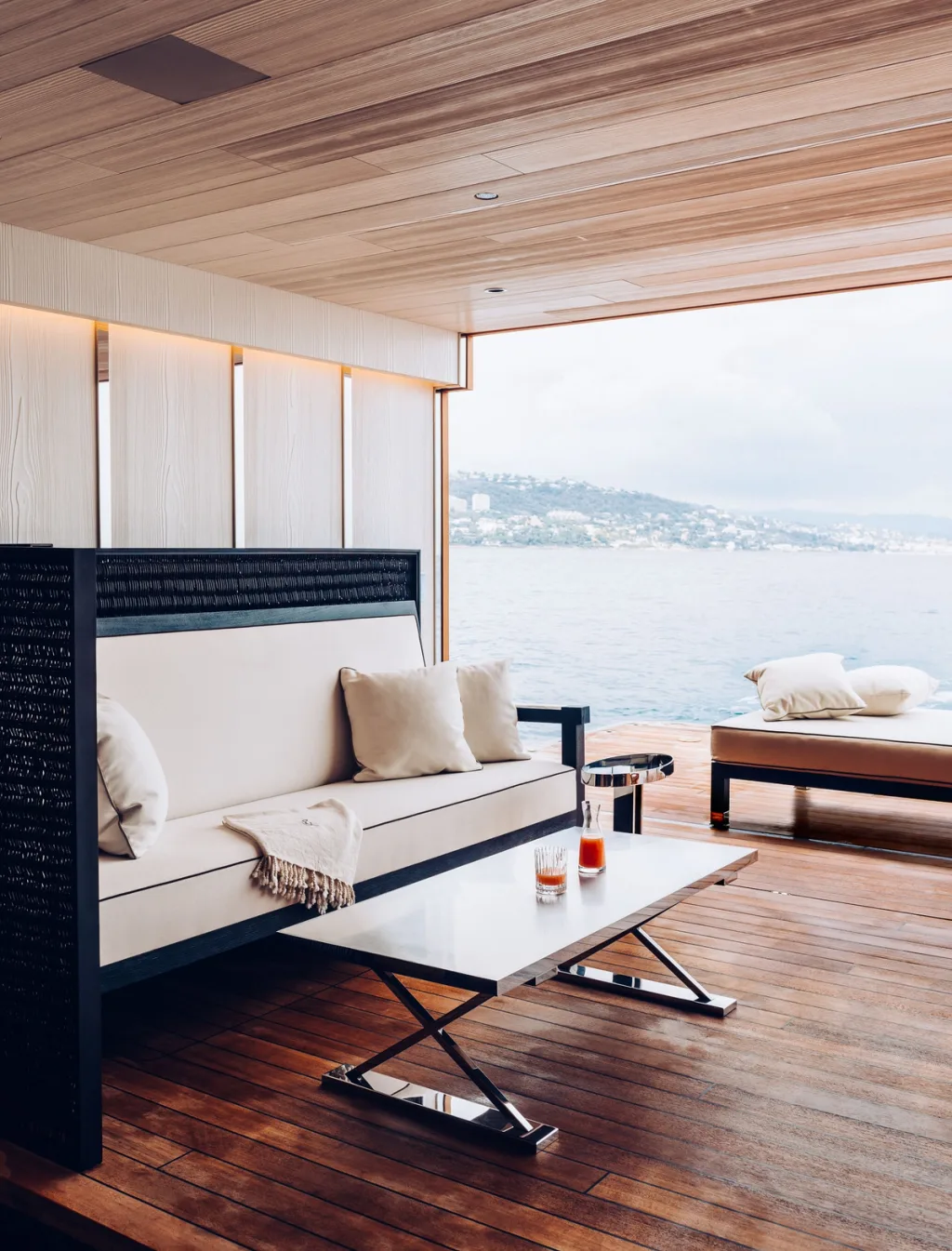 Covered sea-facing lounge with white cushions and a low folding table aboard Atlante
