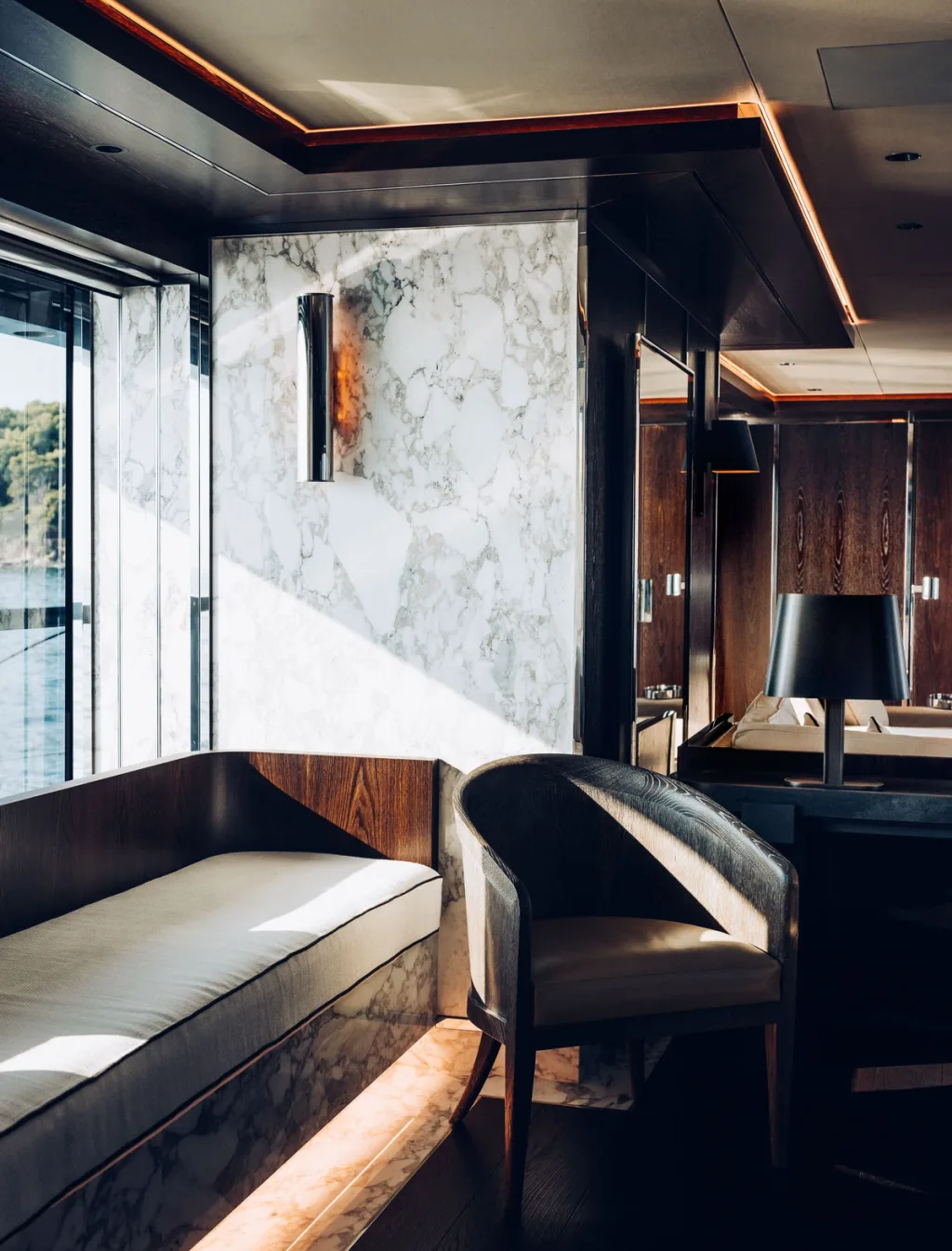 Sunlit curved bench and dark armchair beside a veined wall aboard Atlante