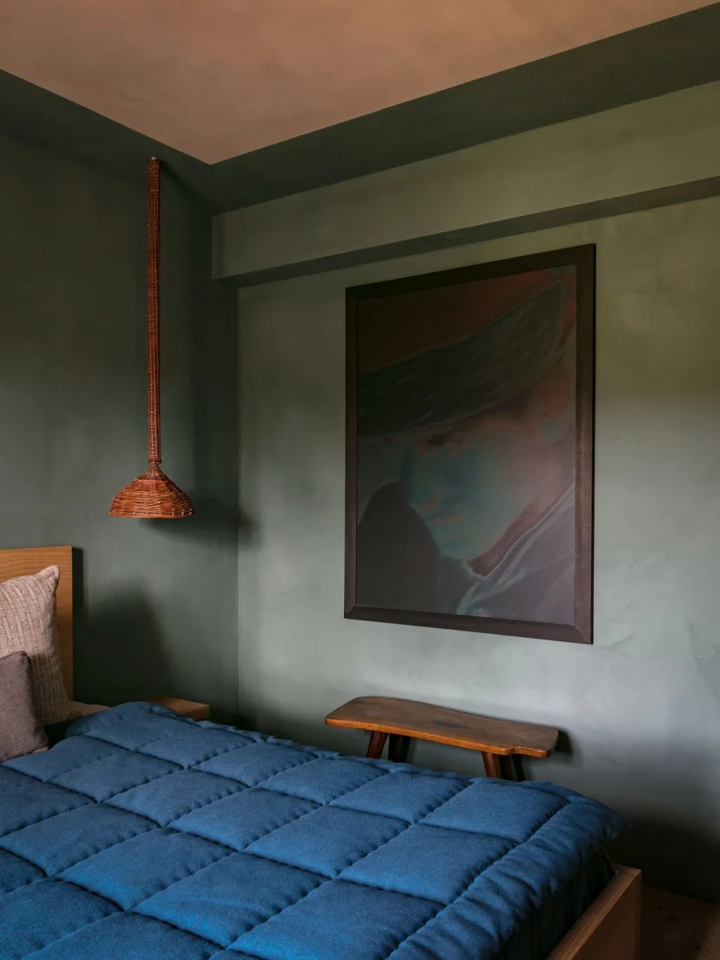 Blue quilted bed and hanging woven lamp against green walls at Fabrègues, Pierre Yovanovitch