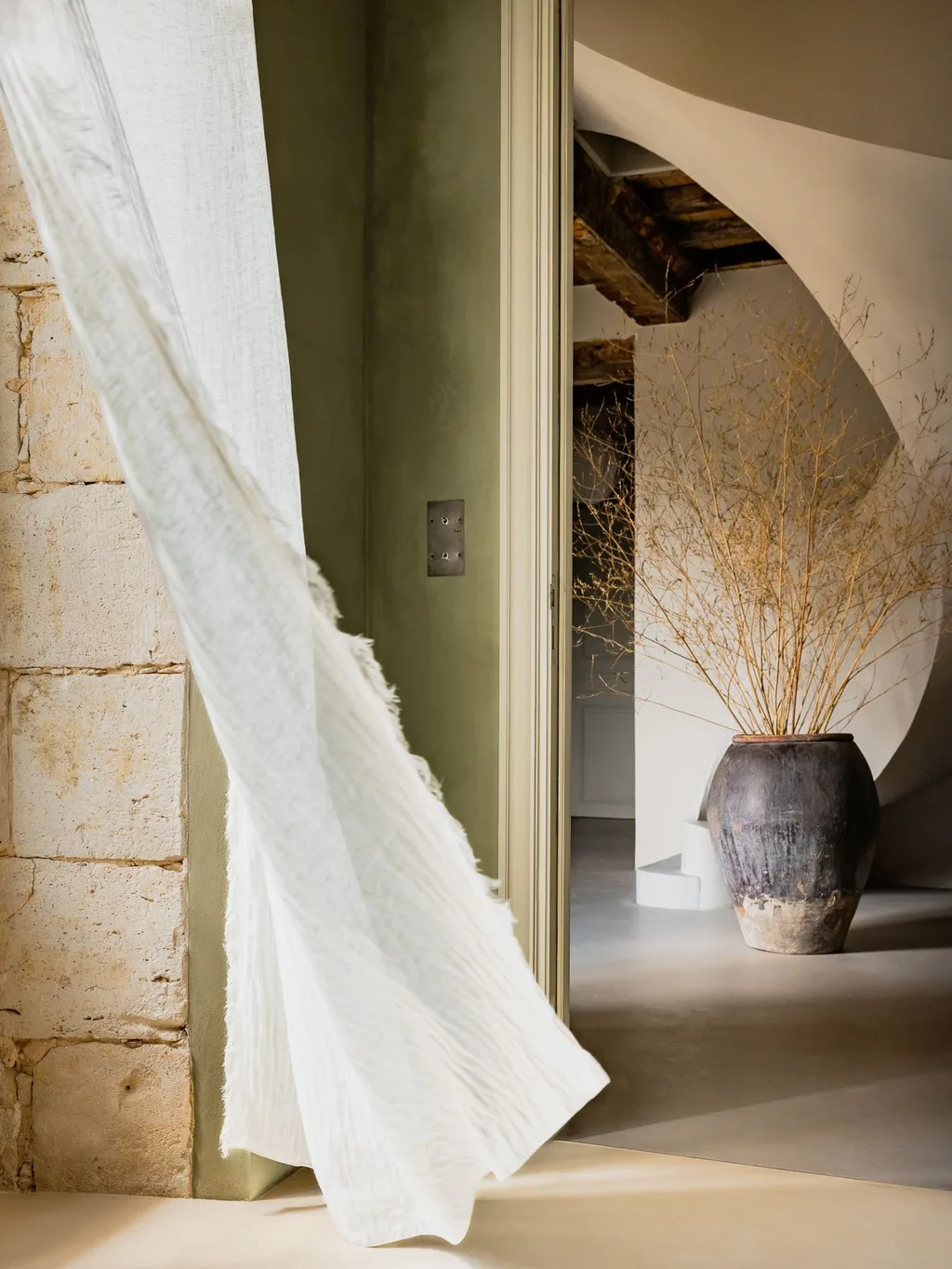 Sheer curtain billows in a stone doorway near the spiral stair, Manufacture Royale de Lectoure hotel