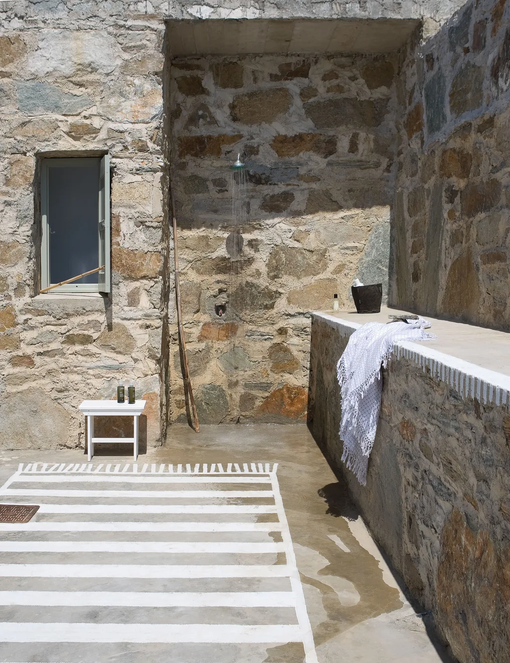 Open-air shower within rough stone walls above a striped painted floor, Paola Navone, Serifos