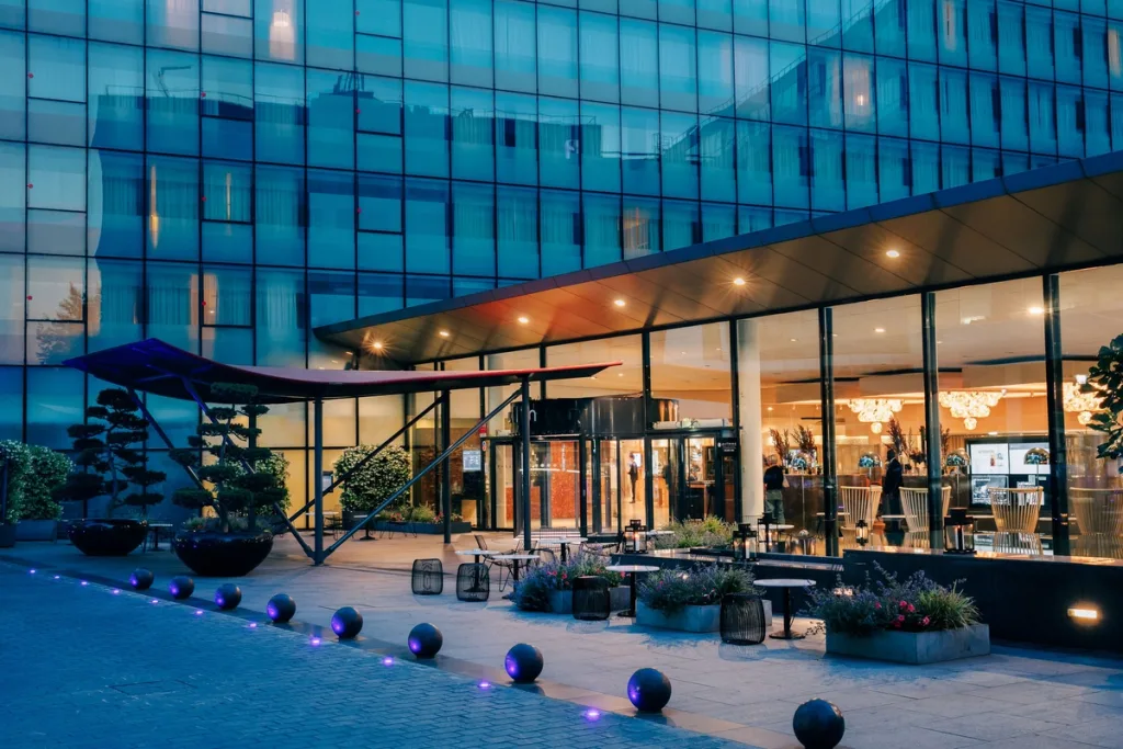 Glass hotel facade glowing at dusk beneath a red canopy entrance, Pullman Bercy hotel