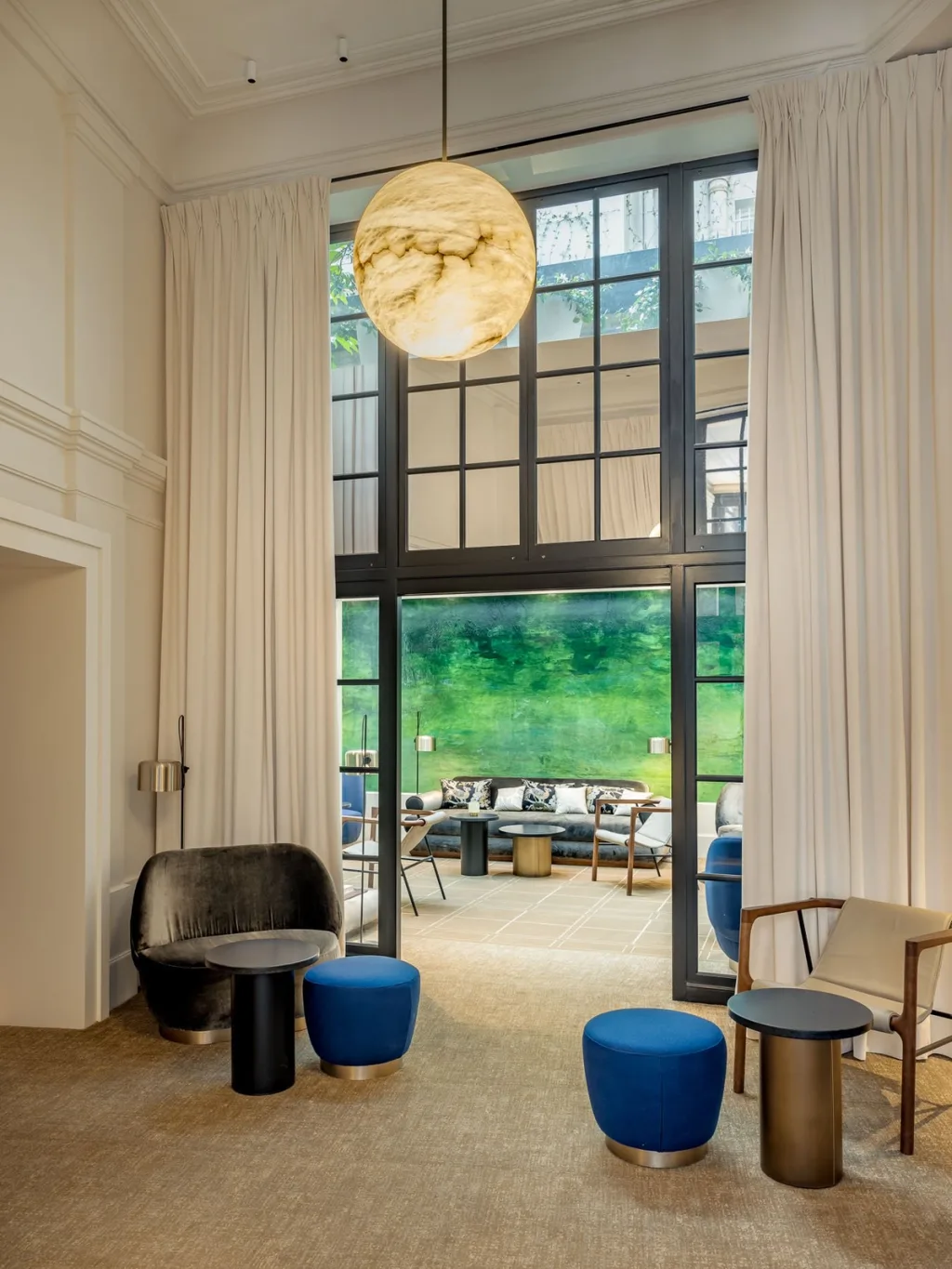Sitting area with tall arched windows and an alabaster globe pendant at Hotel Pavillon St Germain, Paris