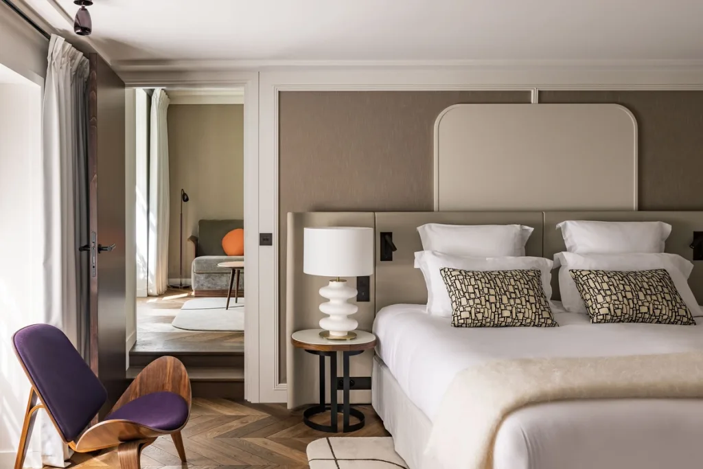 Bedroom with a purple armchair and a sitting room glimpsed through the doorway at Hotel Pavillon St Germain, Paris