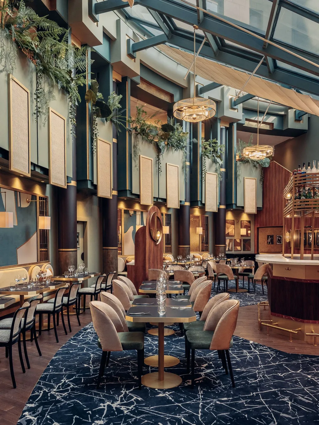 Skylit atrium restaurant with hanging plants, brass pendants and bar, Nest MGallery Hotel, Paris