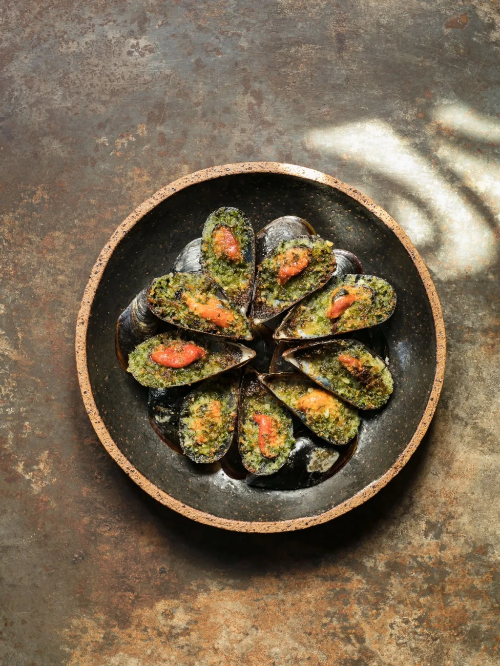 Mussels in their shells with green herb topping on a dark plate for Cyril Lignac’s Saisons cookbook
