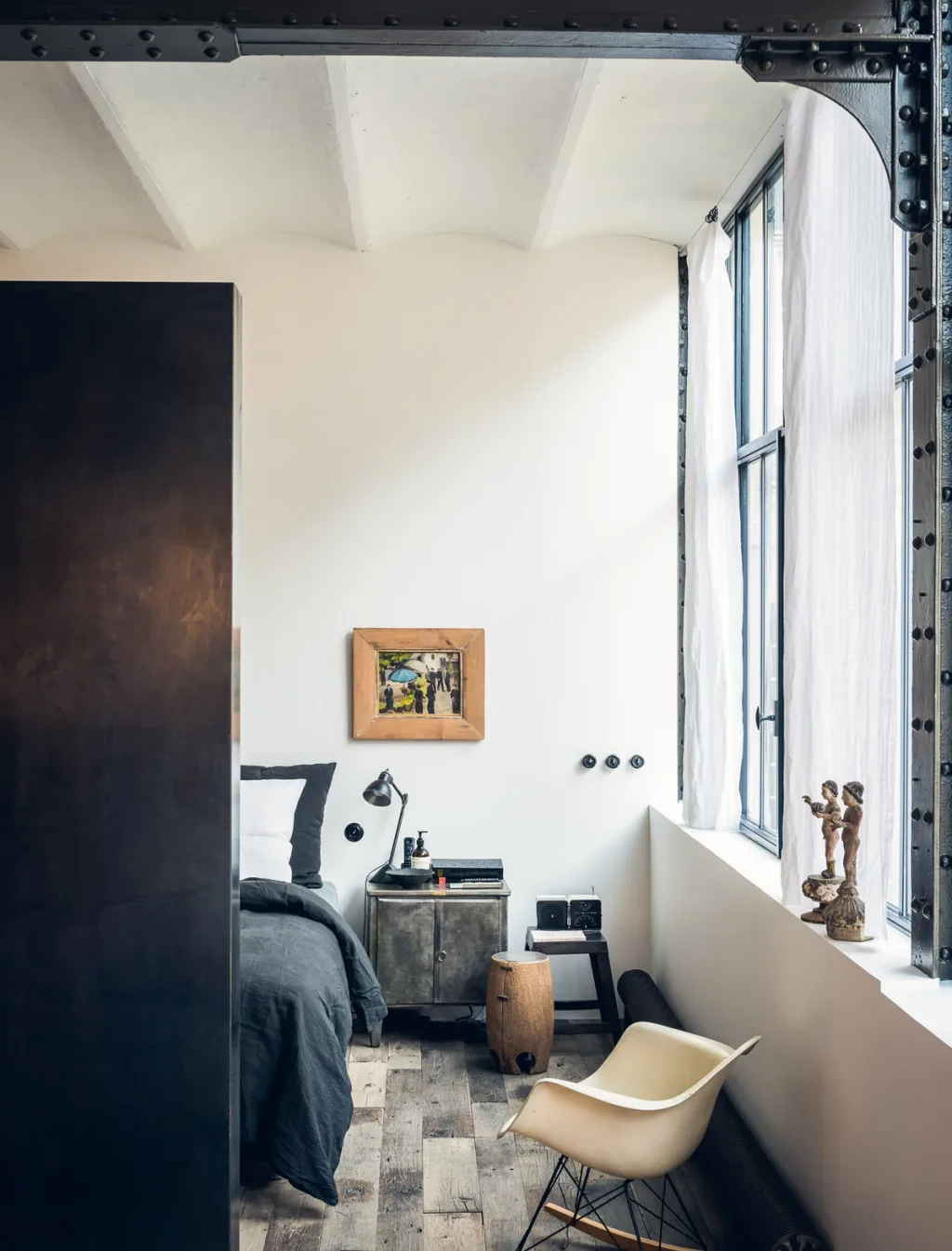 Bright bedroom with industrial beams and a pale rocking chair at Daniel Rozensztroch's Paris home