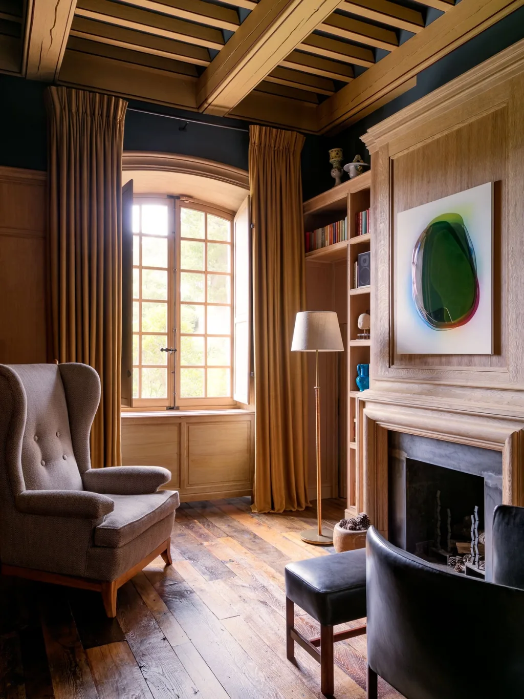 Wingback chair beside a panelled fireplace and tall window at Fabrègues, Pierre Yovanovitch