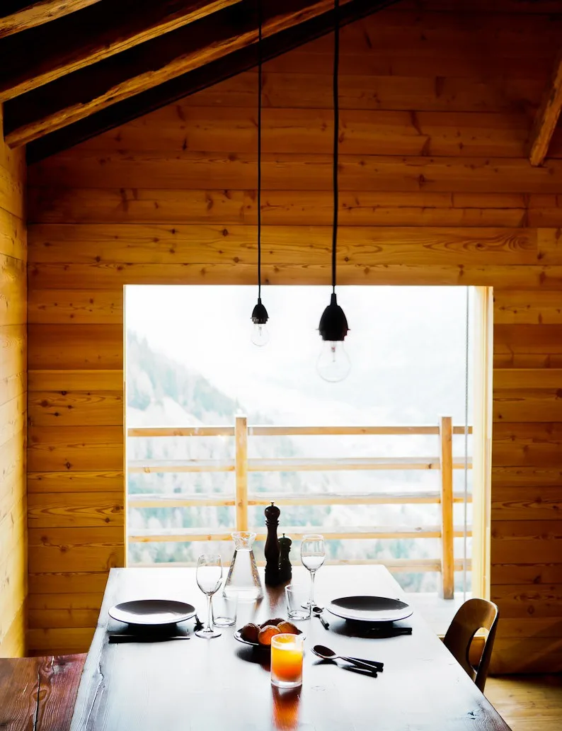 Table set for two beneath pendant bulbs with a mountain view at Montagne Alternative hotel, Switzerland