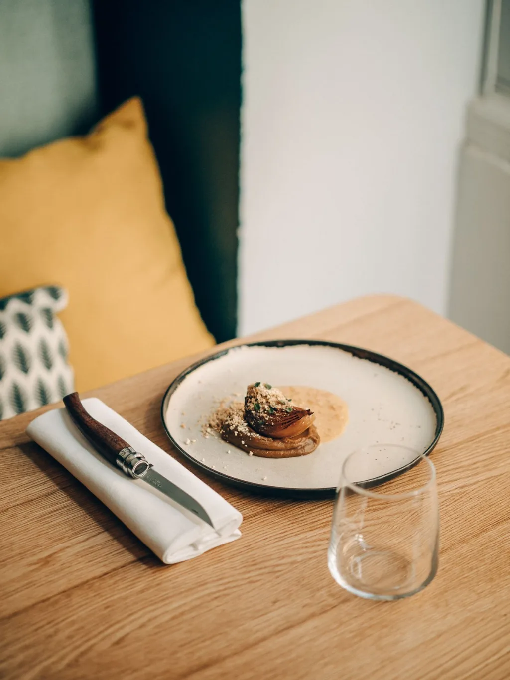 Small plated dish on a wooden table beside a yellow cushion in a Lyon restaurant