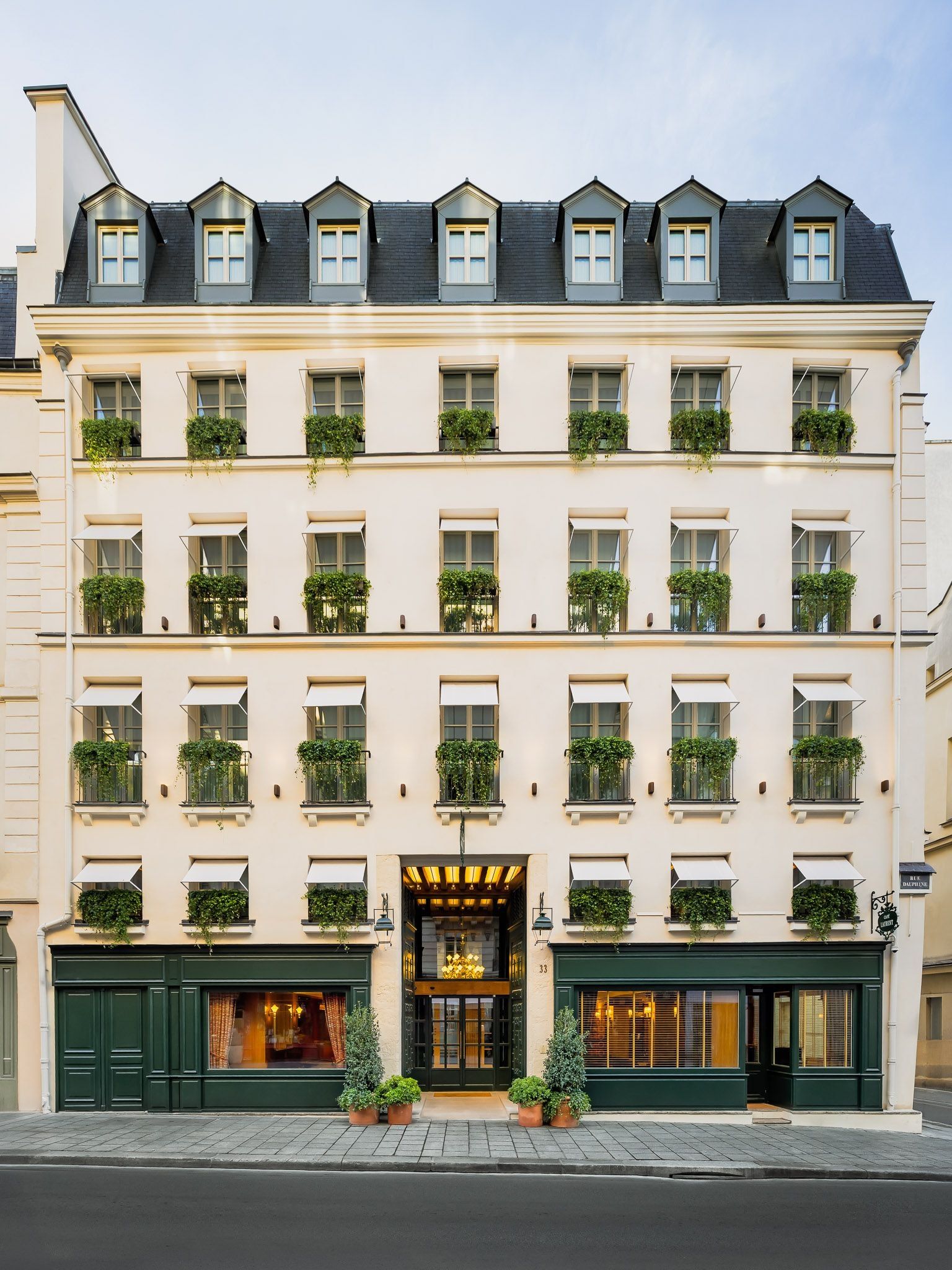 Hôtel d’Aubusson’s pale façade in Paris, with rows of planted window railings, dormer windows and a central entrance between dark green shopfronts.