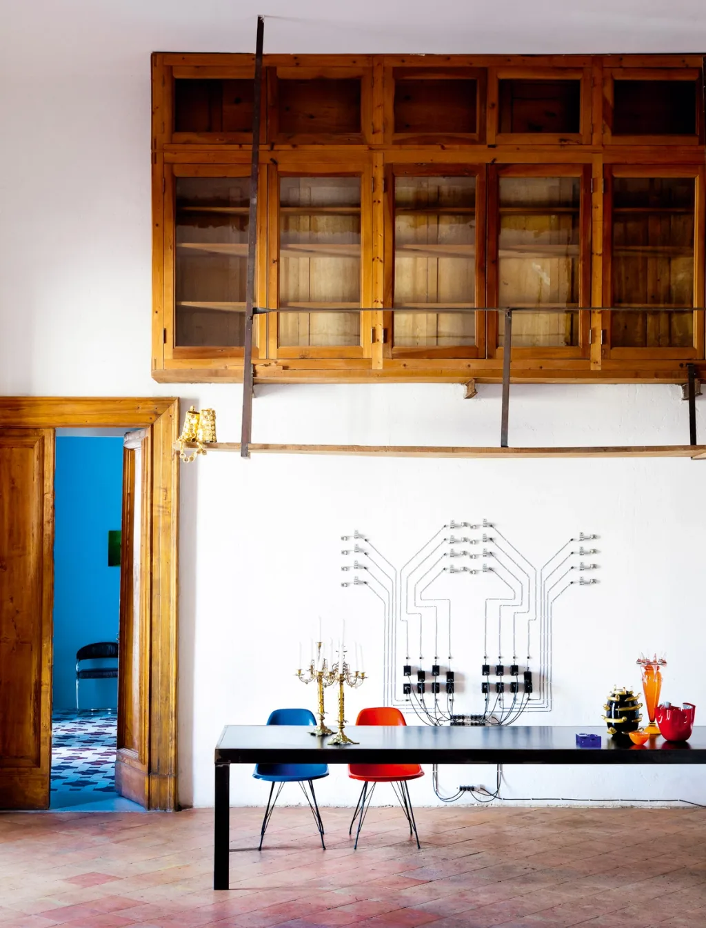 Long table and colourful chairs beneath high wooden cabinets in the Antonio G. Martiniello project, Naples