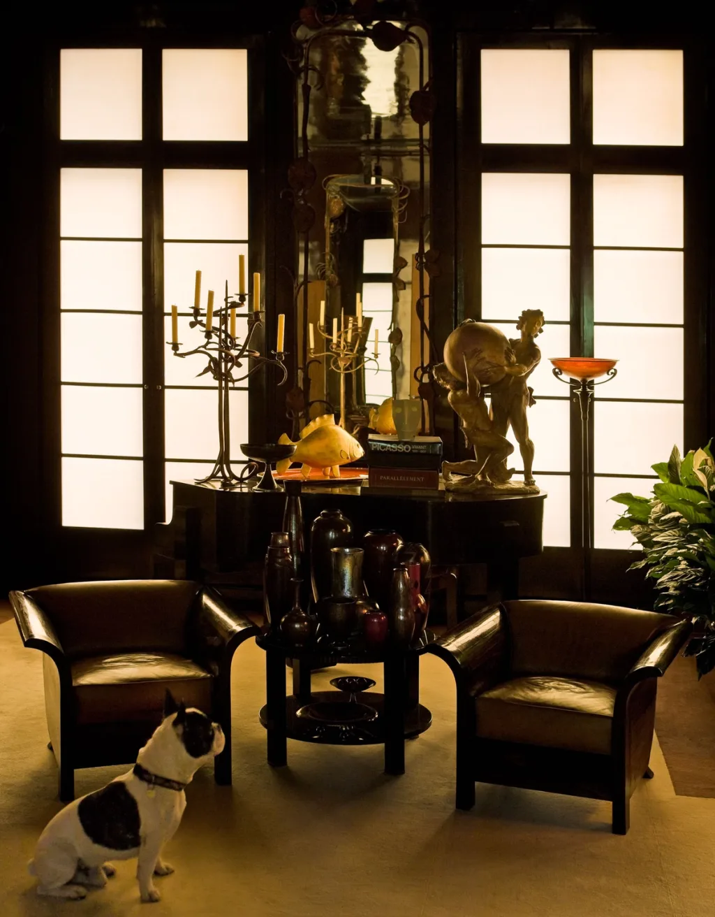 Black-and-white dog beside dark armchairs and a sculpture-filled table, Yves Saint Laurent, Paris