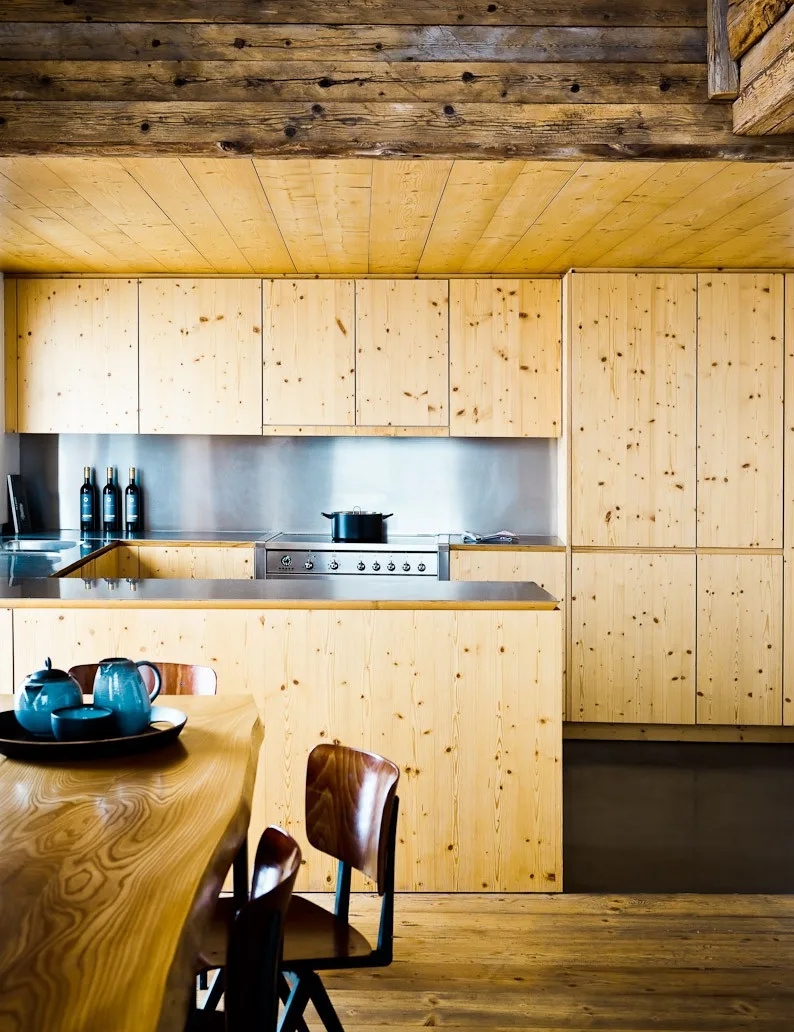 Pale wood kitchen with a stainless stove and a live-edge dining table at Montagne Alternative hotel, Switzerland