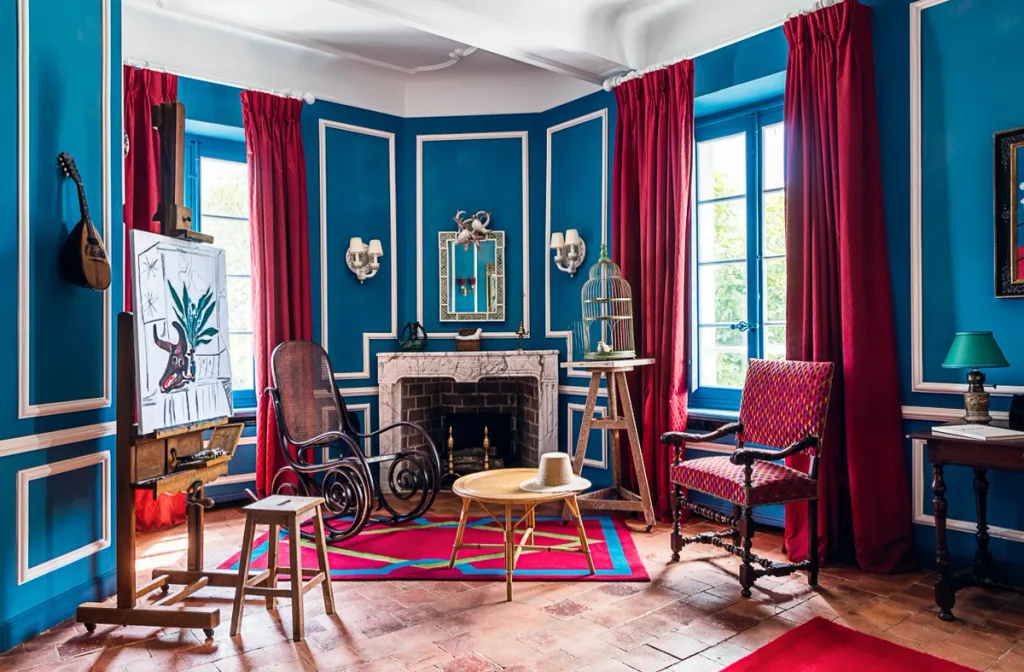 Blue room with red curtains, a rocking chair and painting on an easel at Dior, la Colle Noire
