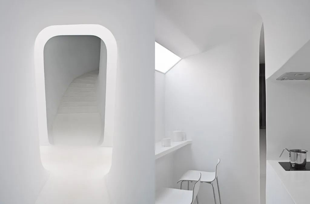 Rounded stair opening beside a compact white kitchen and stools, The Snake by François Roche