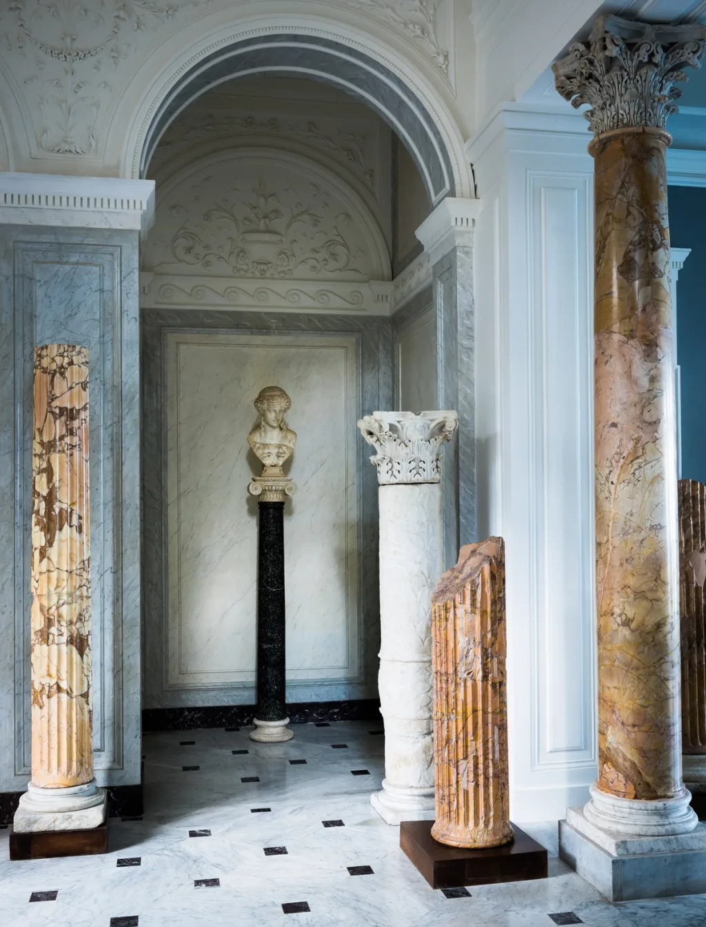 Sculptural bust and freestanding column fragments under a decorative arch at Villa Astor