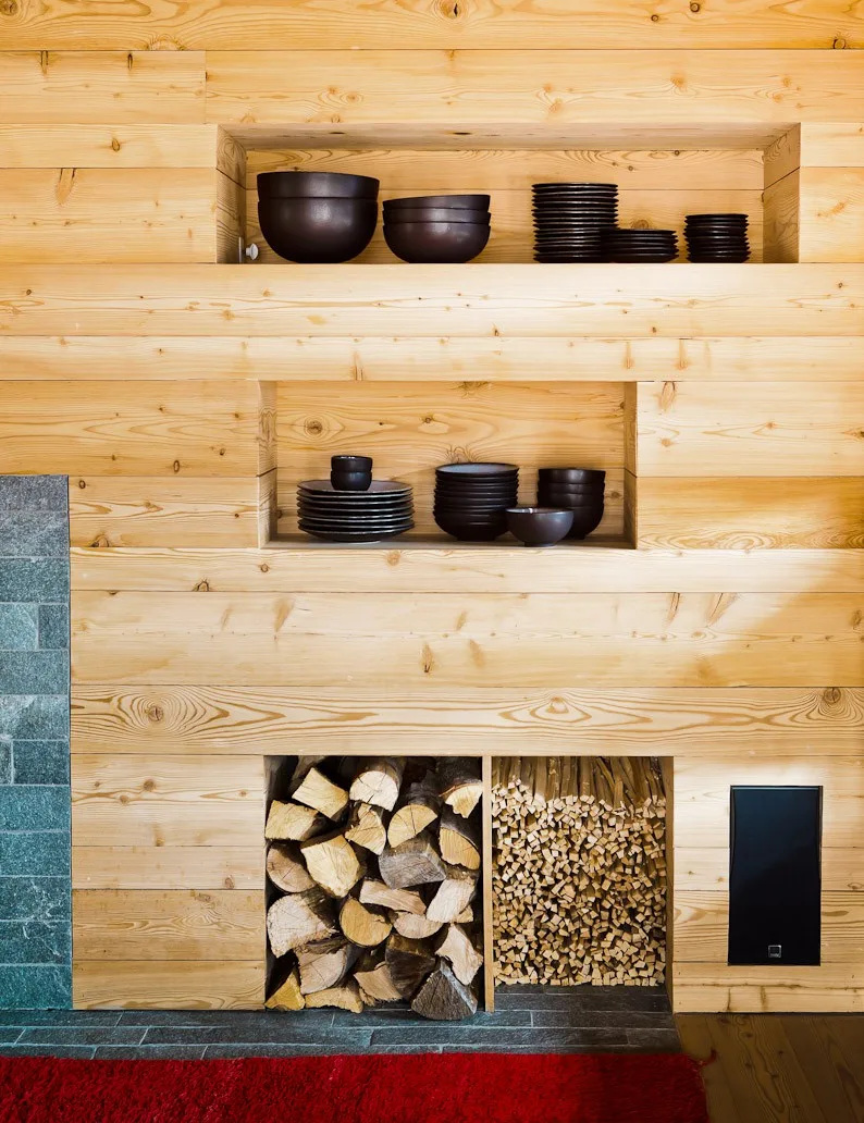 Built-in pine shelving with black ceramic dishware and stacked firewood at Montagne Alternative hotel, Switzerland