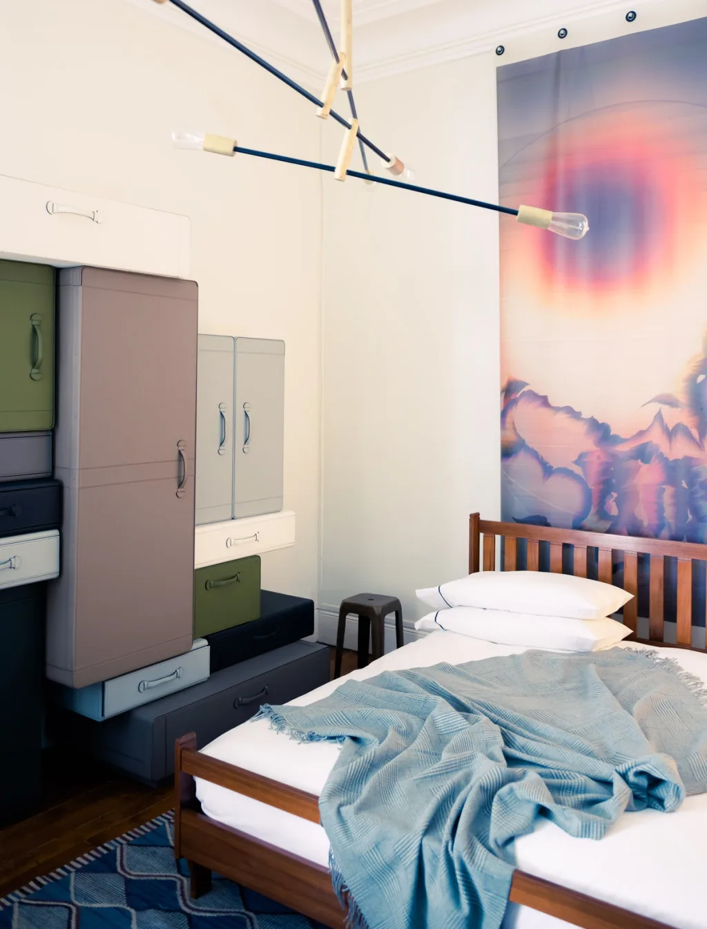 Wooden bed with a blue throw beside stacked multicoloured cabinets, Dimore Studio, Paris